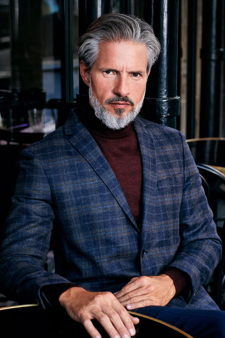 Sergi Puig international senior fashion model color studio photography seated pose navy blue pinstripe suit burgundy wine turtleneck sweater serious intense gaze long silver hair grey beard Salitre Models.
