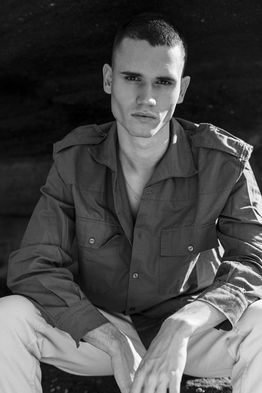 Outdoor portrait of male model Marco Santana wearing an unbuttoned green shirt over light-colored trousers.
