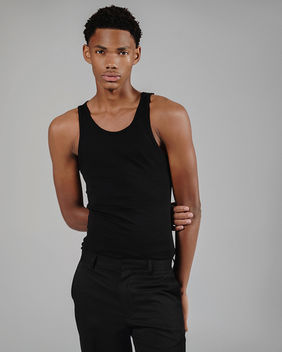 Diptych of agency polaroids featuring male model Amin Glafi in a studio. Showcasing a half-body shot and a full-body shot wearing a black sleeveless tank top and black trousers.