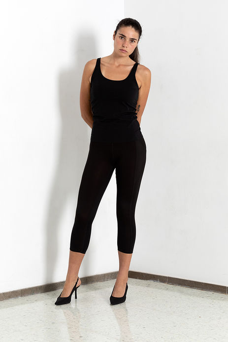 "Full-body model digital photograph of Angie Alvarez in bright white studio. She is standing against a clean background wearing a tight black tank top and fitted black pants, showing her silhouette."