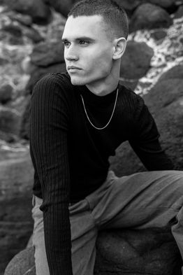 Black and white outdoor portrait of male commercial model Marco Santana wearing a dark sweater and jeans.