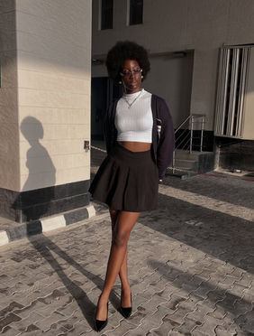 Outdoor street style photograph of tall model Chauntelle Ejiogu in a mini skirt, white tank top, black cardigan, and sunglasses.