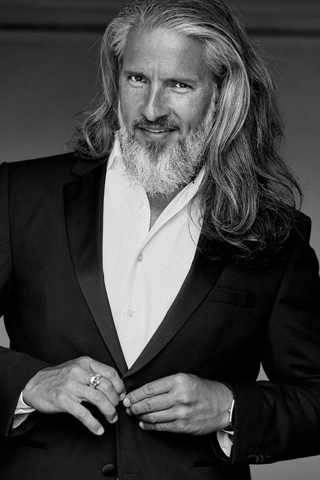 Sergi Puig international senior fashion model black and white photography tailored blazer jacket buttoning gesture long silver hair grey beard high contrast studio portrait formal menswear Salitre Models.