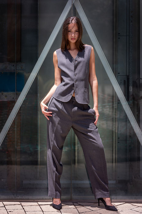 Model Idaira Herrera posing outdoors in a matching suit vest and trousers with a glass elevator mechanism in the background.