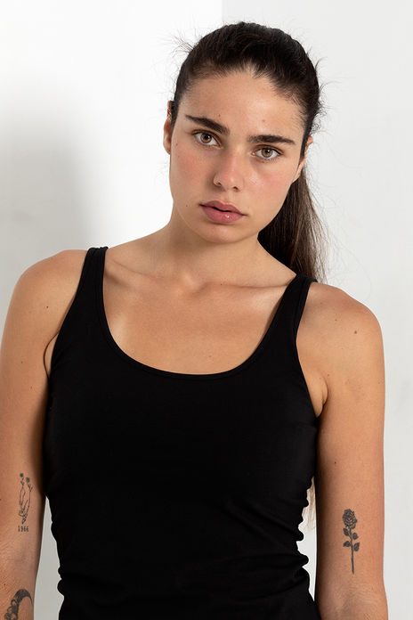 "Full-body model digital photograph of Angie Alvarez in bright white studio. She is standing against a clean background wearing a tight black tank top and fitted black pants, showing her silhouette."