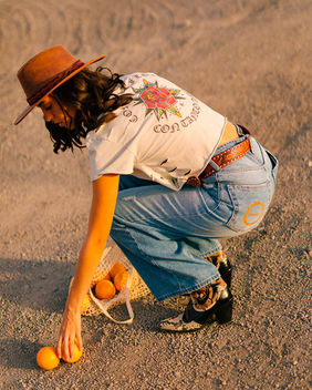 Laura Lopez model Spain sunset countryside editorial wearing denim jeans cowboy boots white t shirt and hat holding oranges Salitre Models