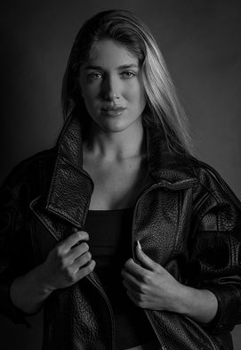 Model Chiara Ayuso posing in a studio wearing a black leather bomber jacket, black tank top, and pleated trousers.