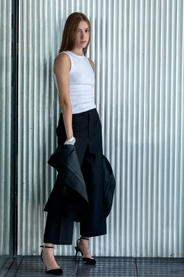 Outdoor portrait of female model Sara Jimenez wearing a black tuxedo jacket and trousers over a white tank top against a neutral background.