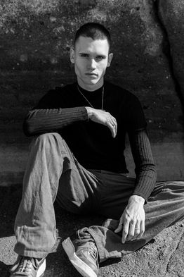 Black and white outdoor portrait of male commercial model Marco Santana wearing a dark sweater and jeans.