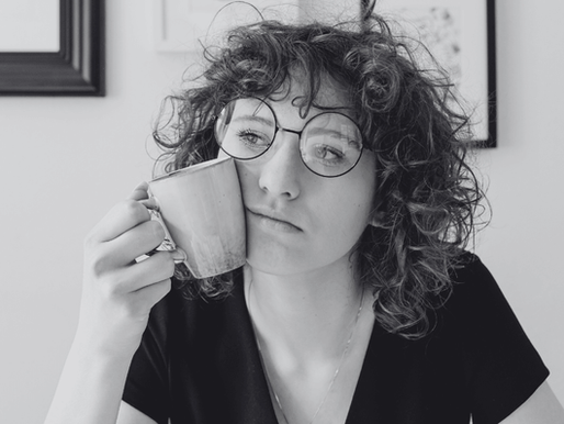 A woman holding a mug in her hand, looking quite glum staring into space thinking about something.