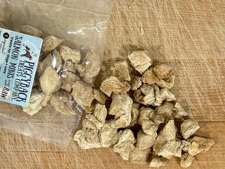 Freeze Dried A package of Wild Caught Salmon dog and cat treats, diced into small pieces, spills across a wooden cutting board.