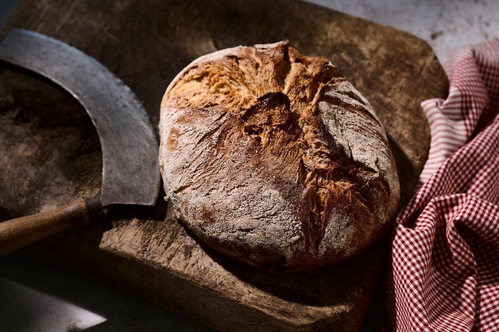 Nærbillede af rustikt brød på træskærebræt med vintage kniv – Redaktionel og kommerciel madfotografi af fotograf Andreas Lampopoulos.
Close-up of rustic artisan bread on wooden board with vintage cutting tool – Editorial & Commercial Food by Photographer Andreas Lampopoulos