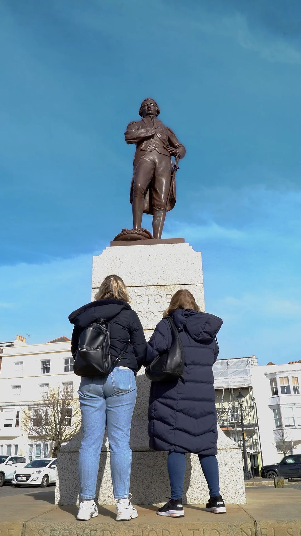 Two women admire a statue against a clear blue sky background.