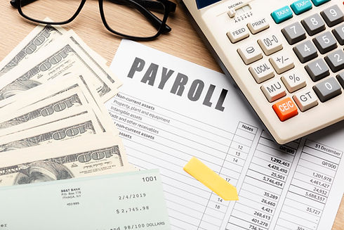 A payroll document surrounded by a calculator, scattered dollar bills, a check, and glasses on a desk, conveying a business and financial theme