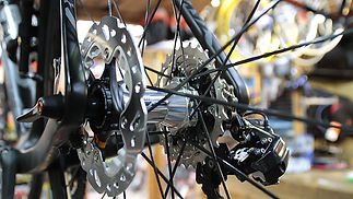 Close-up of a bicycle wheel hub with shiny metal spokes and a disc brake, in a workshop setting