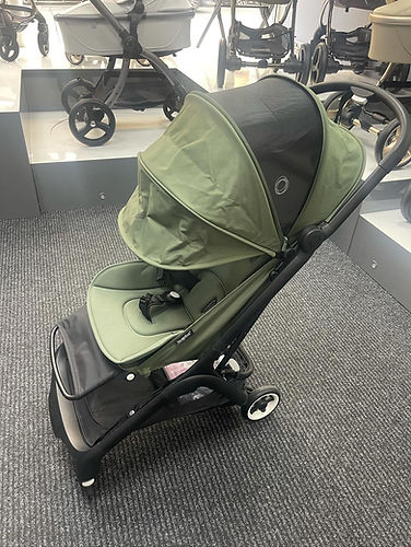 Green baby stroller with a black frame displayed on a gray carpet