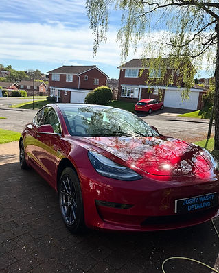 A shiny red car is parked on a suburban driveway under dappled sunlight