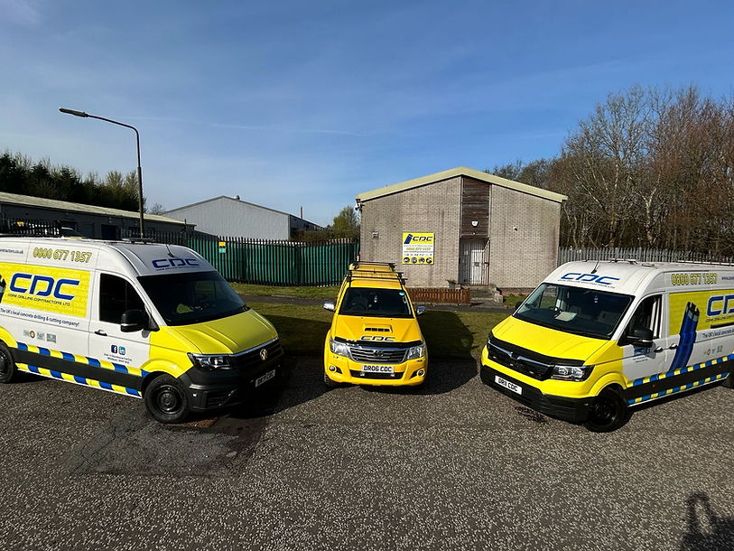 Three yellow and white service vans with blue logos parked in front of a small industrial building under a clear sky