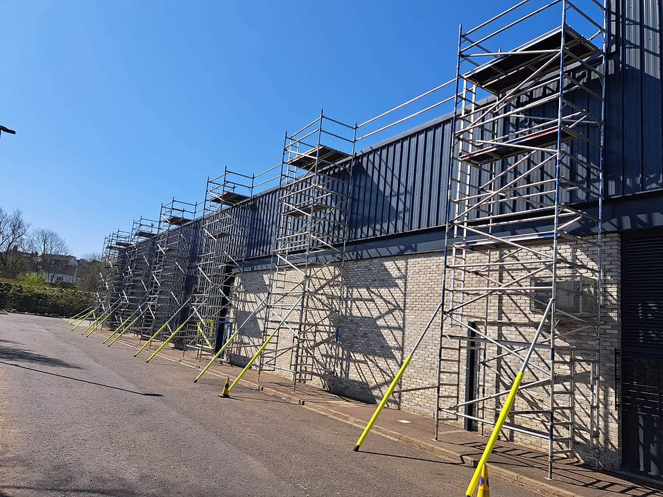 Scaffolding towers mounted on the side of a large, gray, industrial building