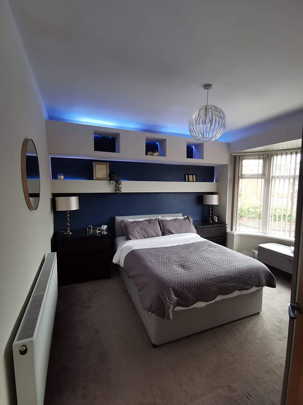Modern bedroom with a cozy double bed, gray bedding, black side tables, blue accent wall, and soft blue ceiling lights