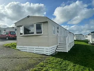 A beige mobile home with white trim sits on a grassy area