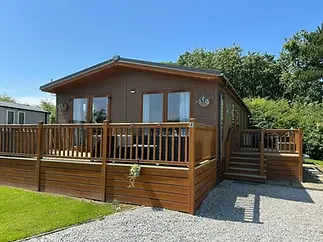 A wooden cabin with a spacious porch, surrounded by greenery