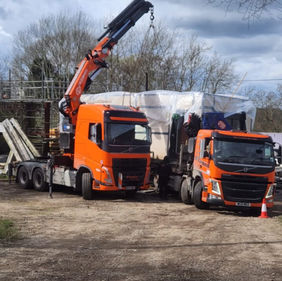 Orange truck with a crane lifting a large gray container in a construction area