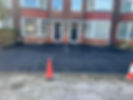 Freshly paved black driveway in front of a brick house with two dark doors and bay windows