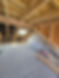 Unfinished attic with exposed wooden beams and insulation, a partially completed brick wall