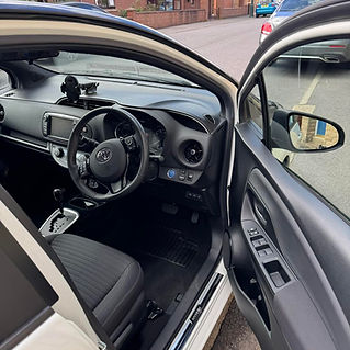 Interior view of a car showing the driver’s seat, steering wheel with a logo, dashboard with a mounted device, and door controls