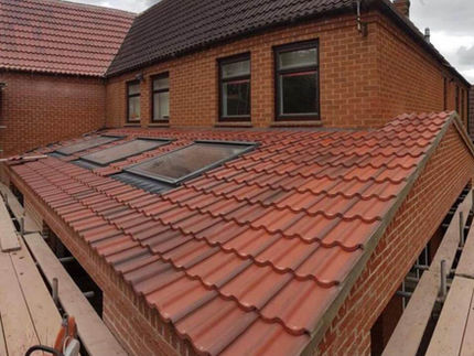 Red brick house with angled red tile roof featuring skylights. Three upper windows have dark frames