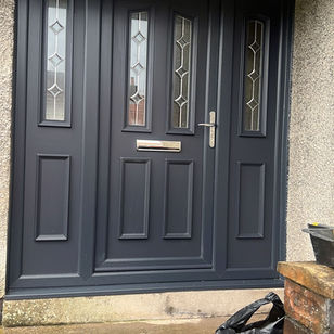 A modern, dark grey front door with decorative glass panels stands at the top of concrete steps
