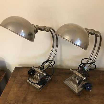 Two vintage metal lamps on a wooden table, featuring curved arms and dome-shaped shades