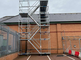 Tall metal scaffolding structure stands against a brick building