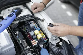 Mechanic's hands working on a car's open fuse box