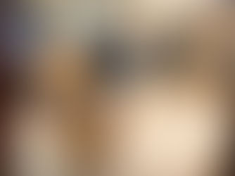 Two yellow Labrador retrievers sit indoors on a brown tiled floor. One dog is smiling. Black sofas are in the background. Cozy atmosphere.