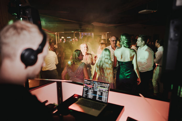 Alexander Stahl aka STEEL als Hochzeits-DJs von hinten über die rechte Schulter fotografiert. Im Hintergrund tanzen die Gäste auf einer Hochzeit. Fotocredit: Kevin Behn.