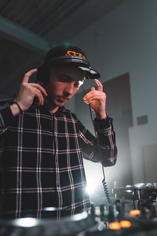 STEEL als DJ bei der Semesterstartparty der Westfälischen Hochschule in Gelsenkirchen. Er hat Kopfhörer auf dem Kopf und macht mit den Händen die Bewegung, als wolle er sie abnehmen. Fotocredit: Jonas Diener.