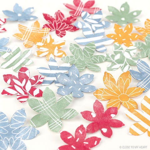Assorted colorful paper flowers arranged on a white surface, each featuring unique patterns and vibrant shades of red, blue, green, yellow, and orange