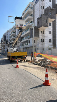 התקנה וחיבור של עמודי תאורה ע"י צוות חשמלאים עם מנוף סל בשכונה חדשה בעיר בישראל