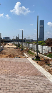 הקמת שדרת עמודי תאורה ברחוב חדש. ברקע בניין משרדים גבוה, ושמיים כחולים ועננים לבנים