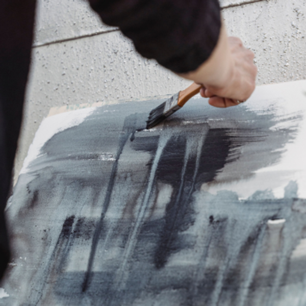 A brush laying grey watercolour strokes on paper