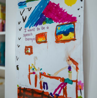 Child’s drawing on the wall that reads ‘I want to be a speech therapist,’ with colorful illustrations.