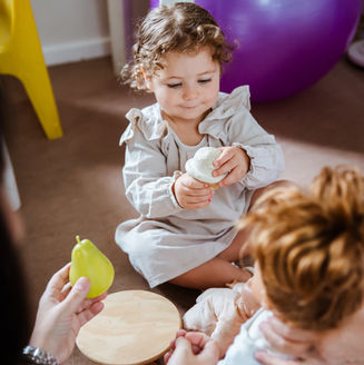 A young girl playing with dolls as two therapists provide speech and language support