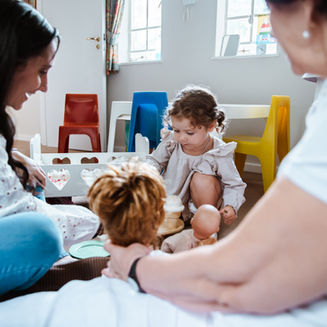 Mother–daughter speech therapy team sitting on the floor with a young girl, using dolls during a session.