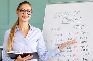 Happy French teacher explaining foreign language rules near blackboard indoors and smiling