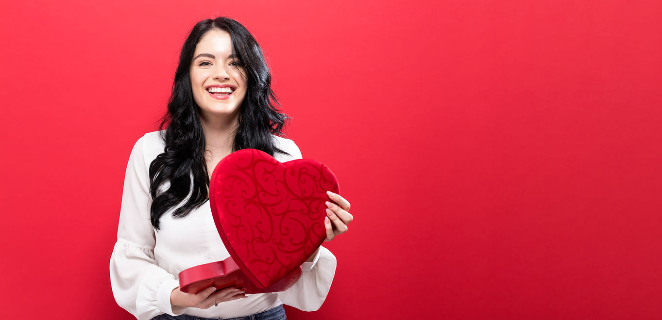 Smiling young woman opening a heart shaped box of chocolates.