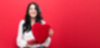Smiling young woman opening a heart shaped box of chocolates.