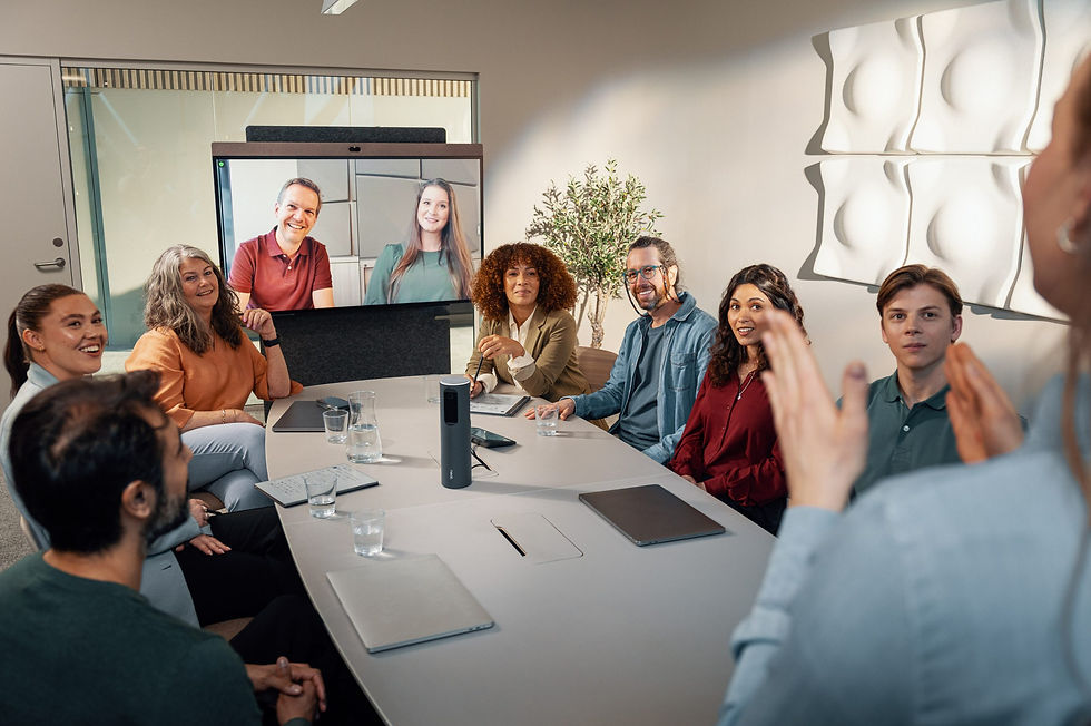 Moderne møterom med åtte personer samlet rundt et ovalt konferansebord under et hybridmøte. En stor skjerm montert på stativ viser to deltakere via videokonferanse. Midt på bordet står en Neat Bar Pro-konferanseenhet. Deltakerne smiler og ser engasjerte ut. Rommet har lyst, minimalistisk interiør med dekorative akustikkpaneler på veggen og en grønn plante i bakgrunnen.