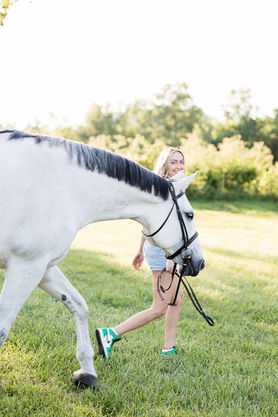 Brandi Cyrus leading her gray hunter jumper horse through a field in Franklin, Tennessee at her show barn, Hunters Court Stable